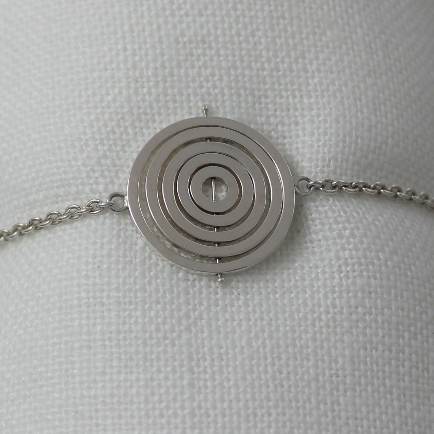 Sterling silver kinetic bracelet with 5 concentric recycled square wire rings on central pin attached to trace chain on sides