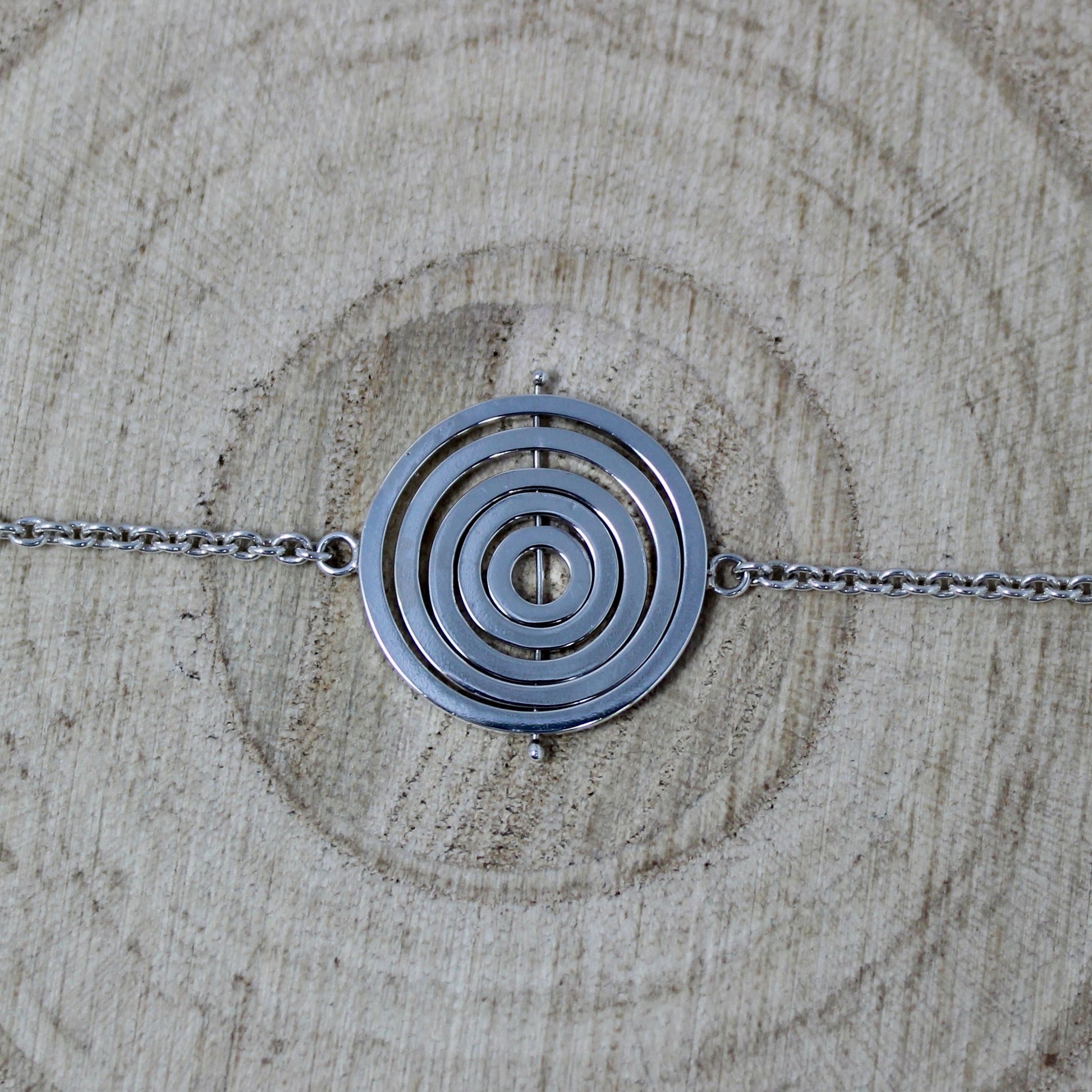 Handmade kinetic silver bracelet with 5 concentric recycled wire rings on central pin, attached to trace chain on each side