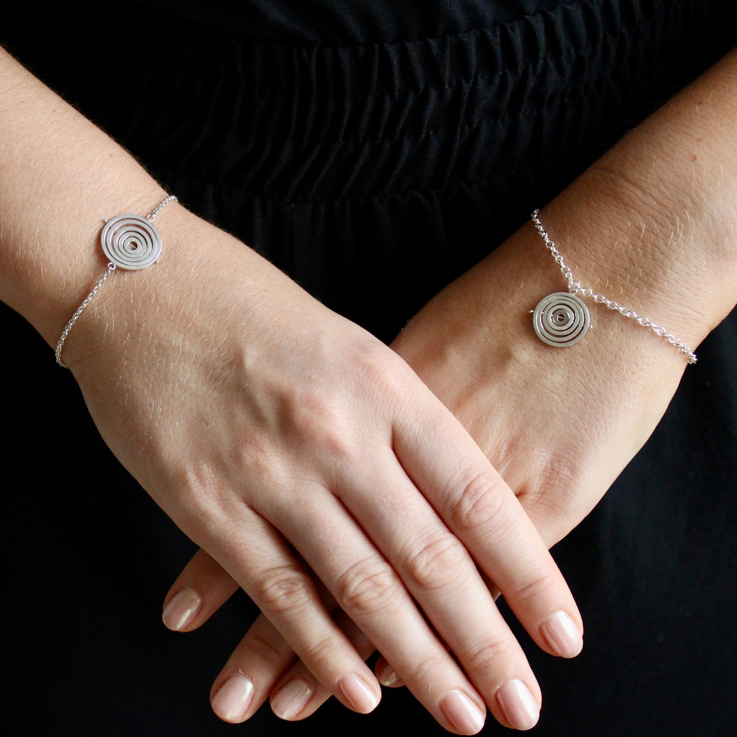 Model wearing 2 styles of sterling silver kinetic bracelets with dainty trace chain and concentric rings held by central pin