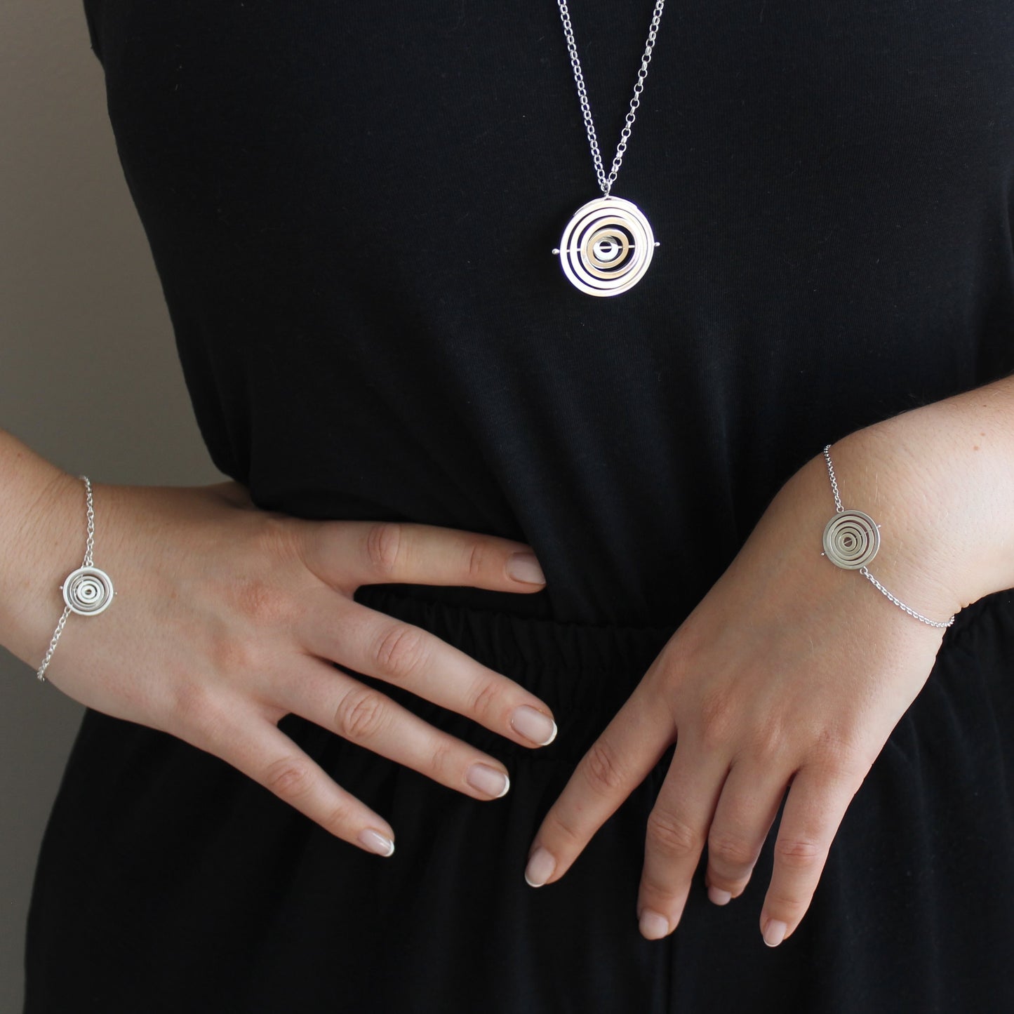 Model wearing hallmarked silver kinetic concentric circles pendant hanging below bust & matching dainty bracelets in 2 styles