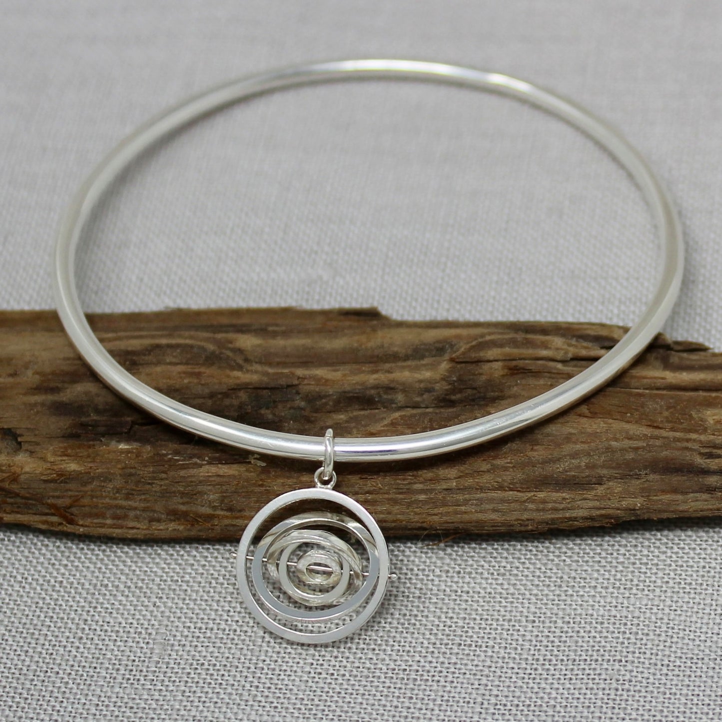 Hallmarked sterling silver handcrafted bangle with dangling kinetic charm made of 5 concentric rings pivoting on central pin