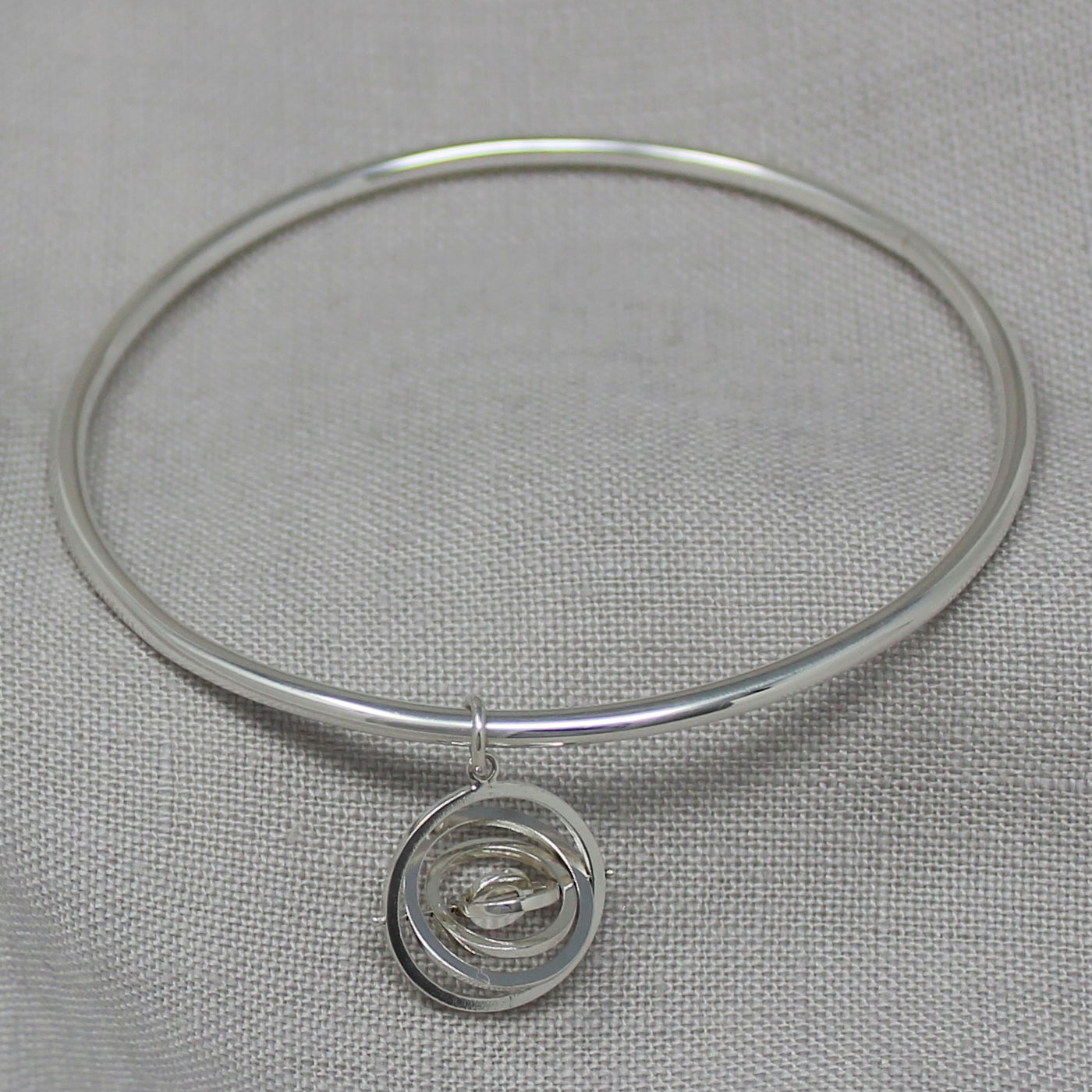 Hallmarked sterling silver handcrafted bangle with dangling kinetic charm made of 5 concentric rings spinning on central pin