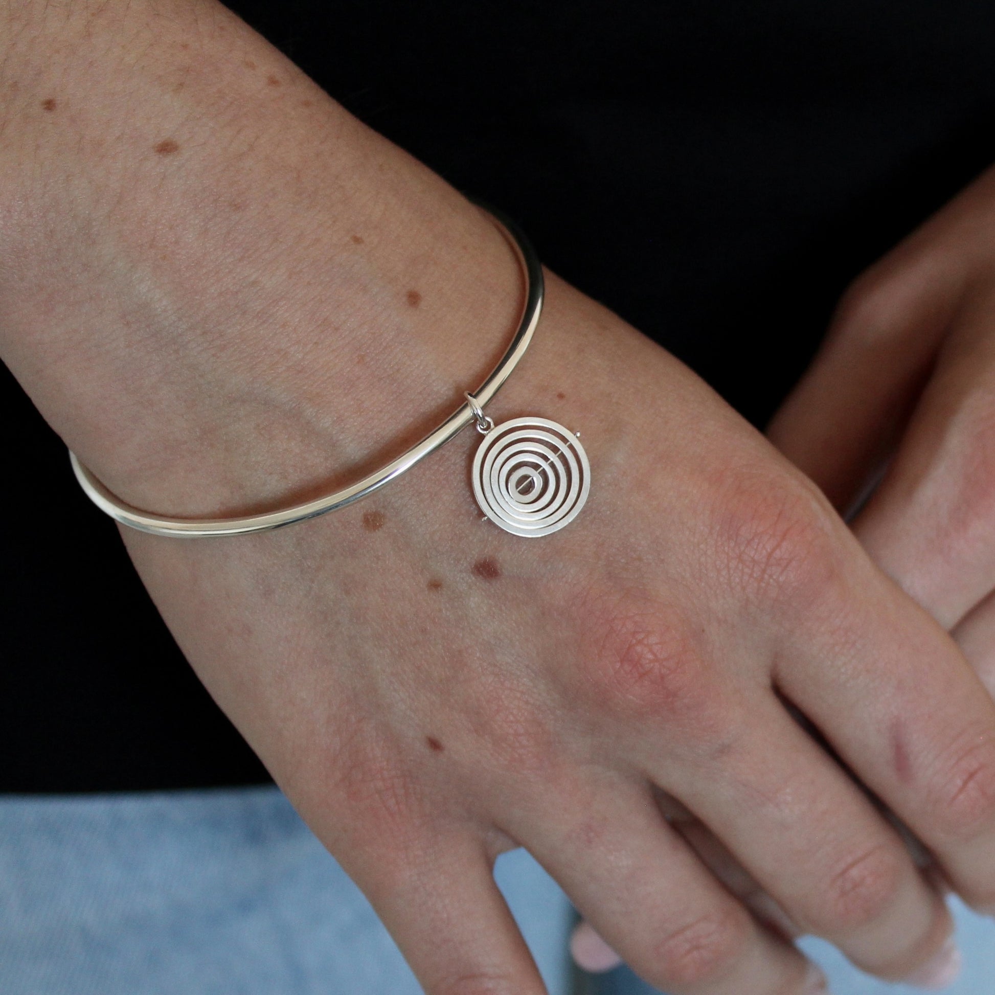 Model wearing hallmarked sterling silver bangle with handcrafted kinetic concentric circles charm dangling from jump ring