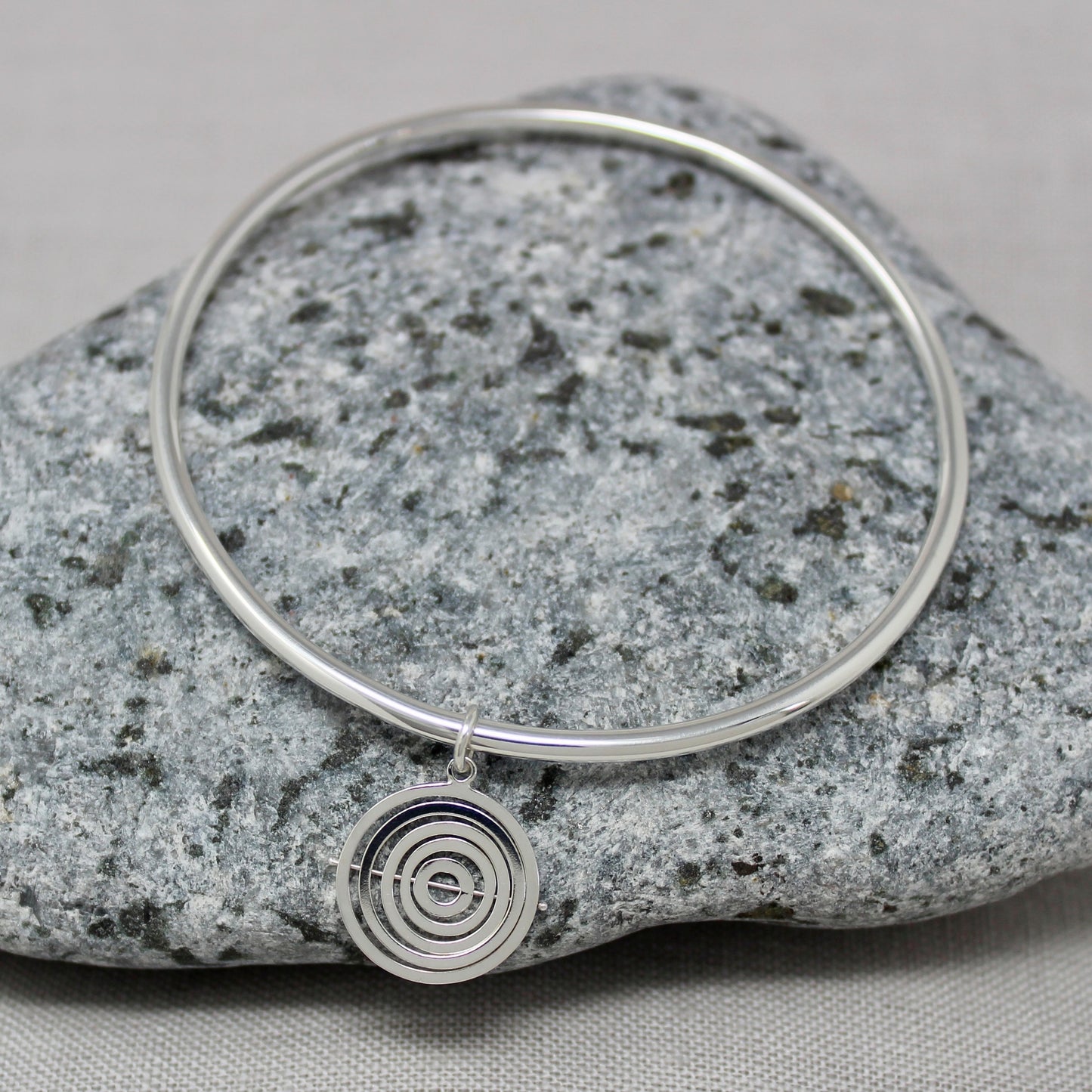 Handmade recycled silver 1.5cm wide kinetic charm with concentric square wire rings held by central pin, on hallmarked bangle