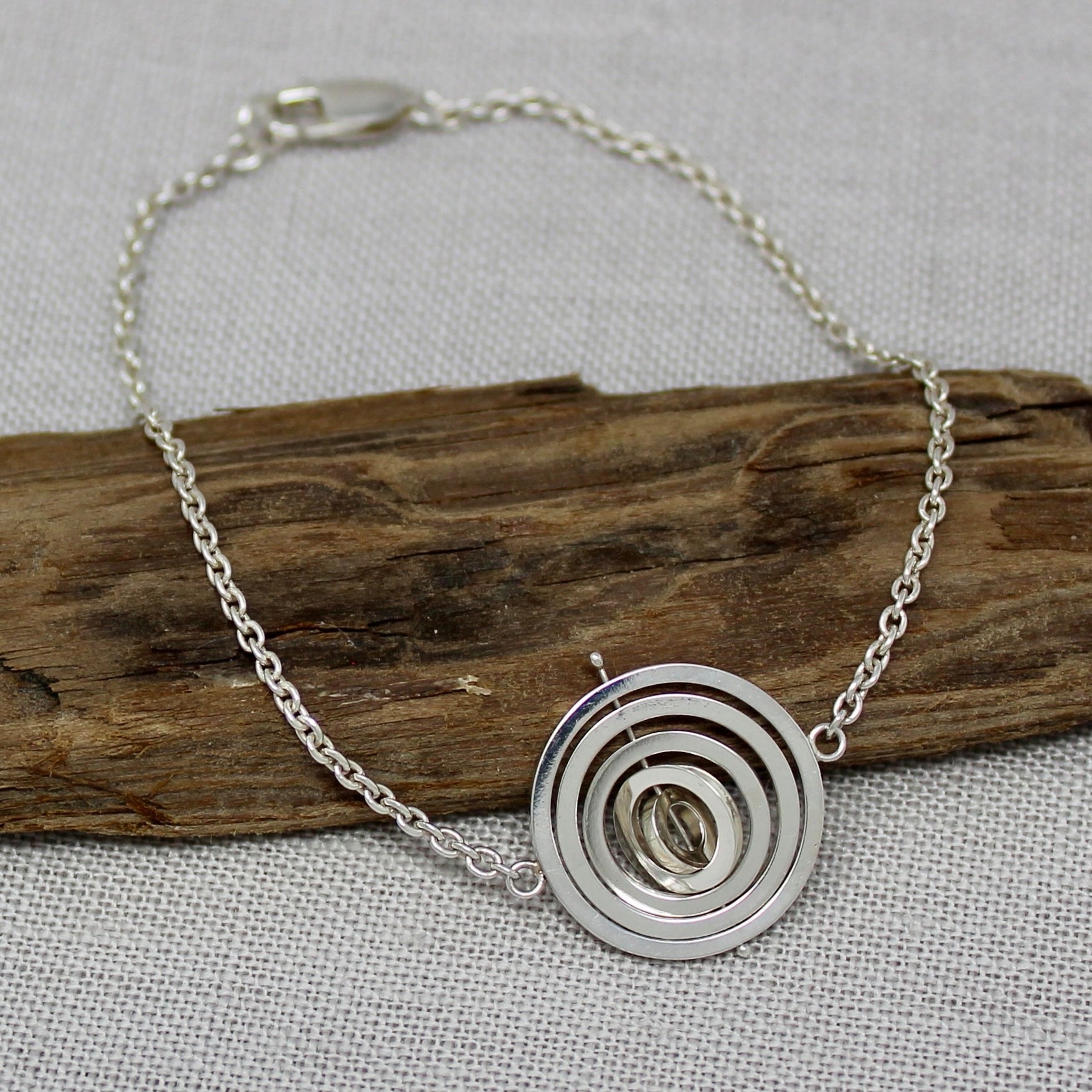 Handmade recycled silver kinetic bracelet, trace chain holding 5 concentric rings pivoting on central pin with lobster clasp